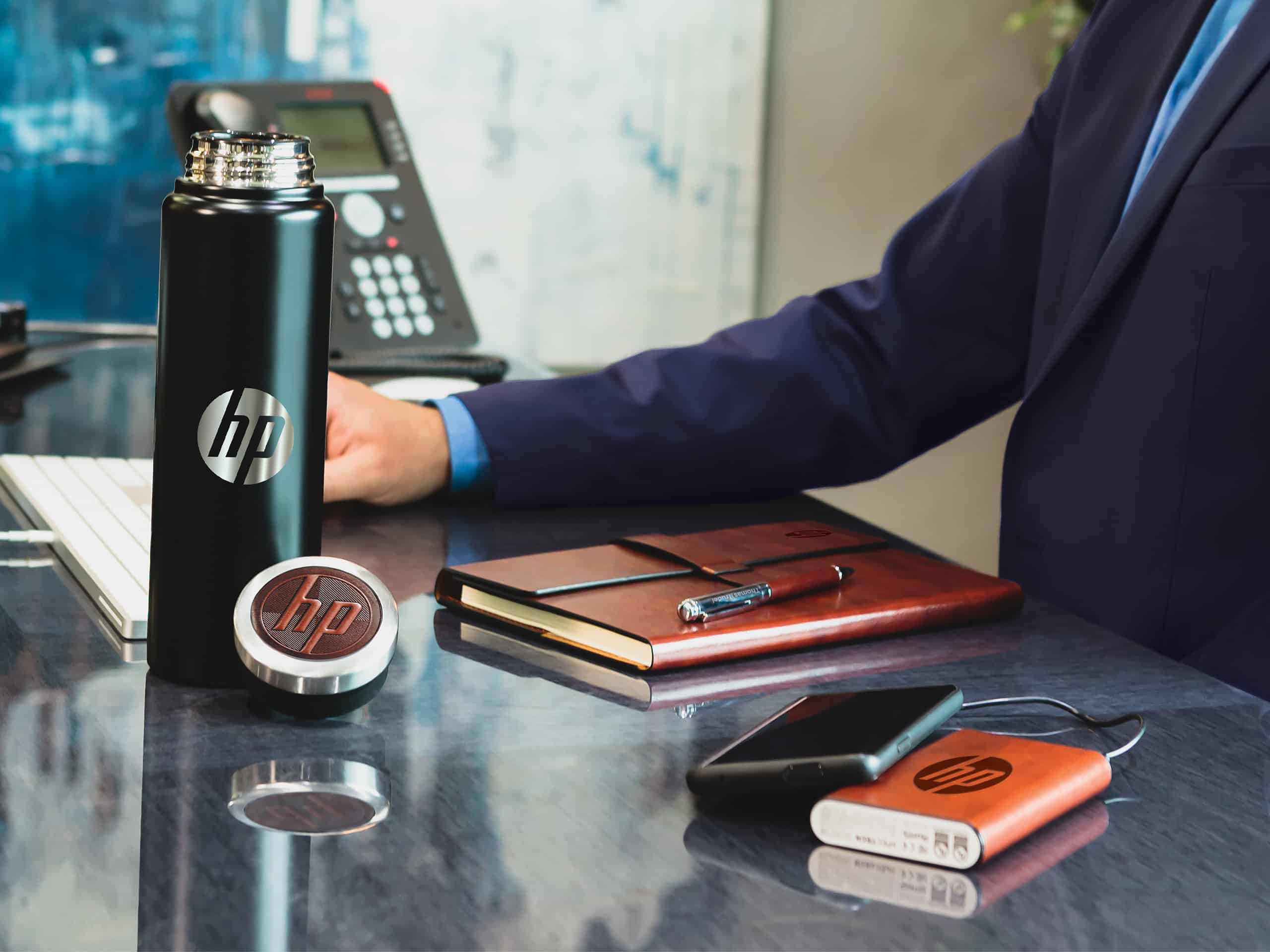 A man in a suit is sitting at a desk with a hp branded water bottle and a power bank.