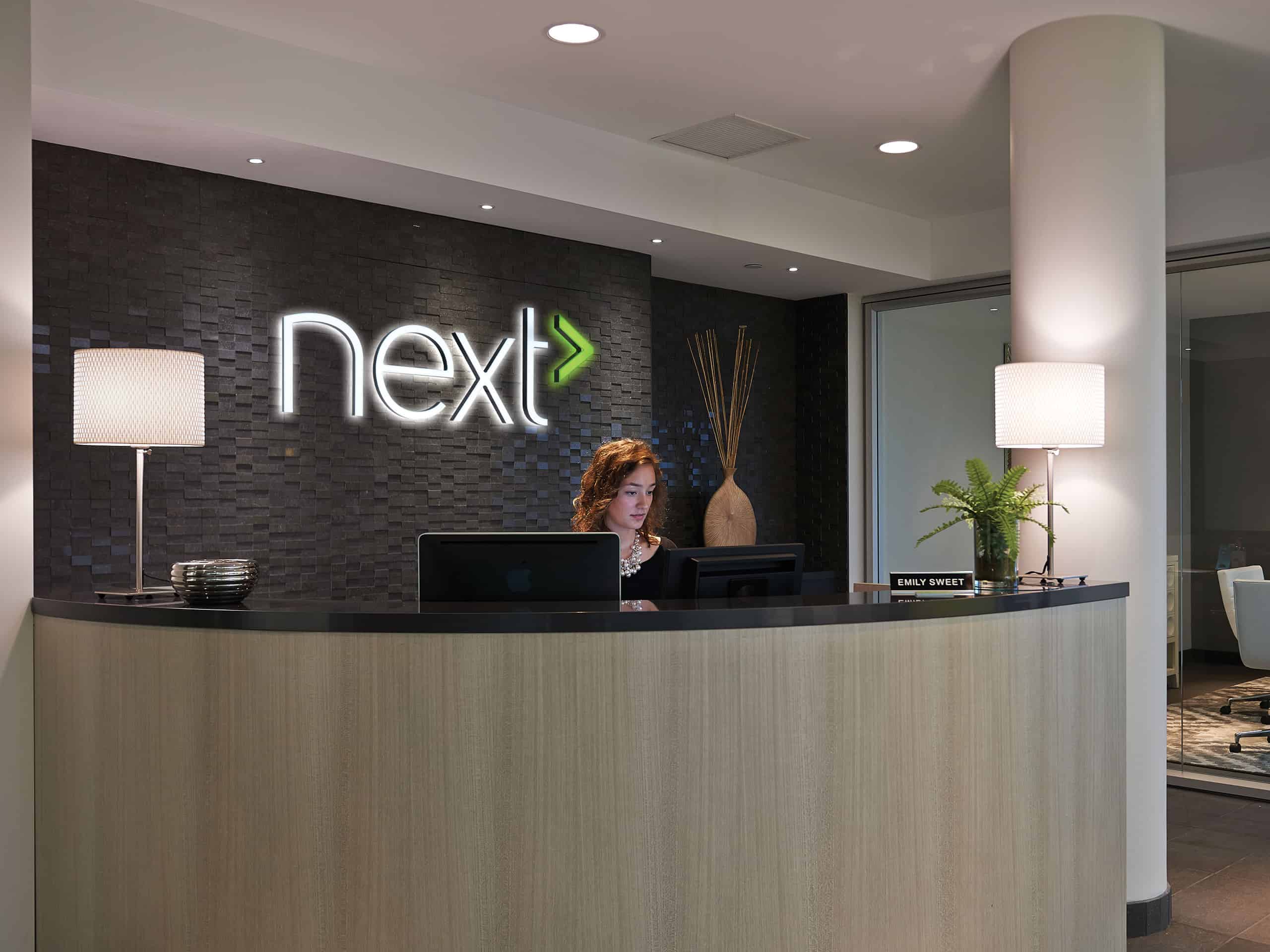 A woman is standing at the front desk of a next hotel.