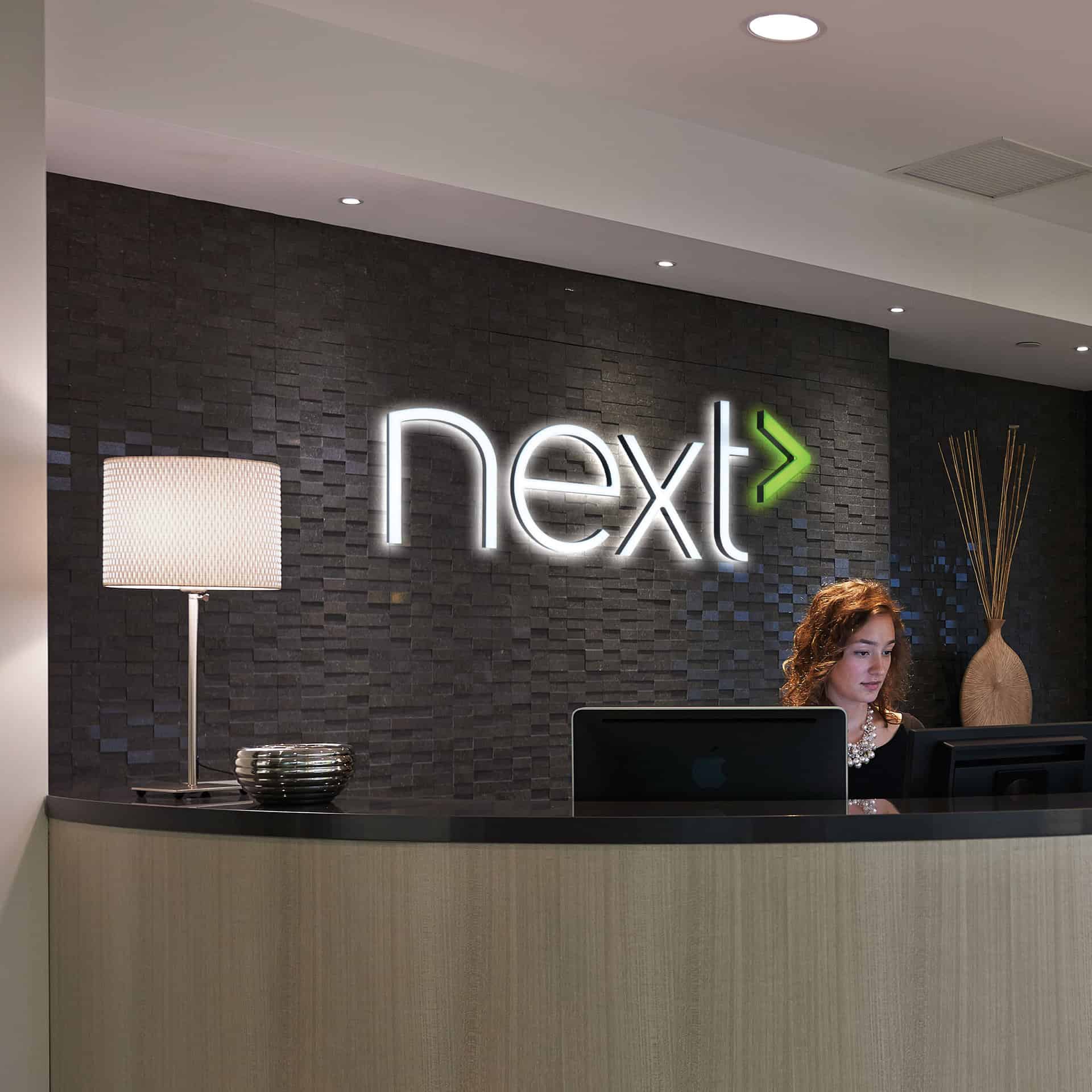 A woman at a reception desk featuring corporate signage behind her.