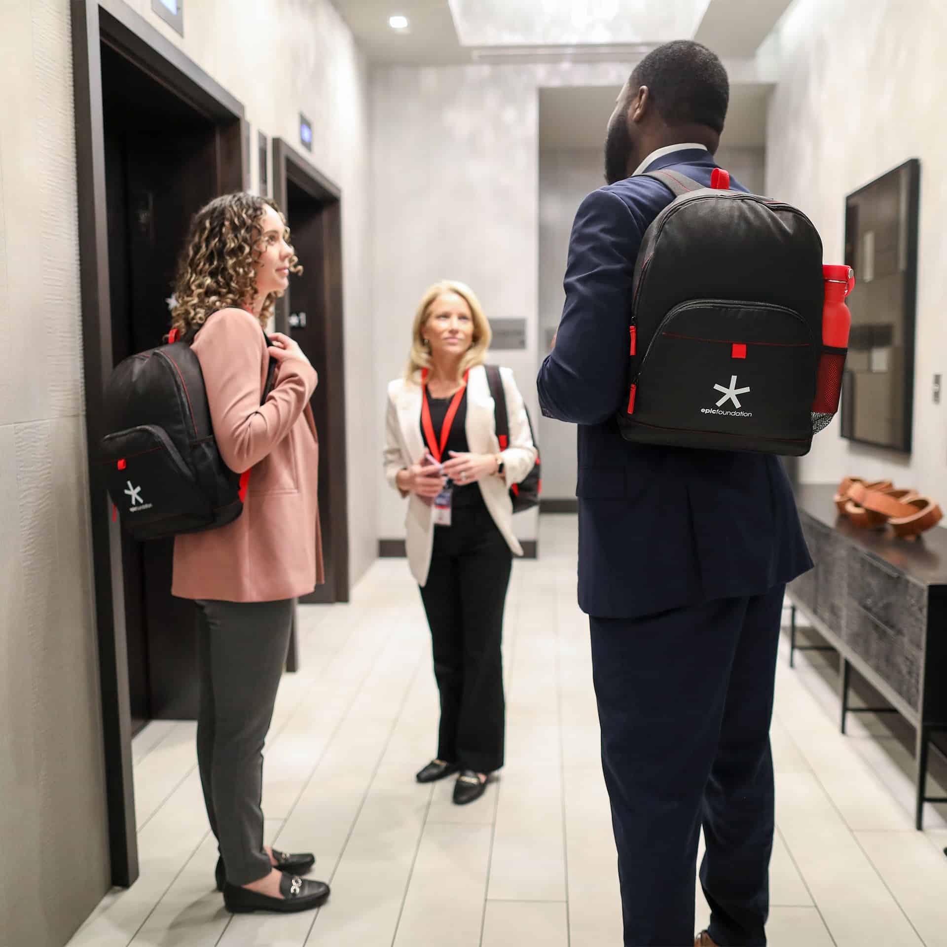 A group of people wearing promotional backpacks standing in a hallway.