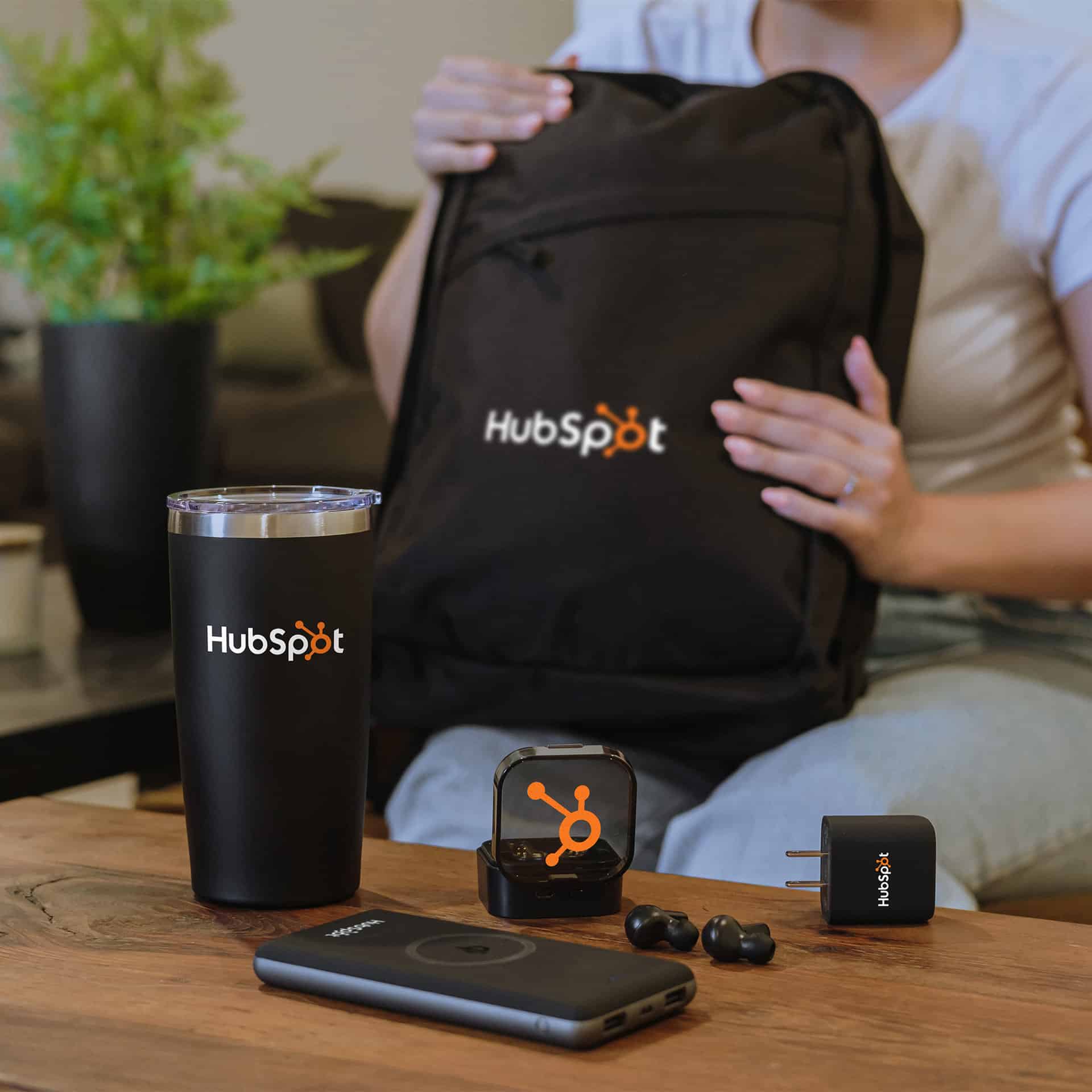A woman is sitting on a couch with a HubSpot branded promotional products backpack and phone.