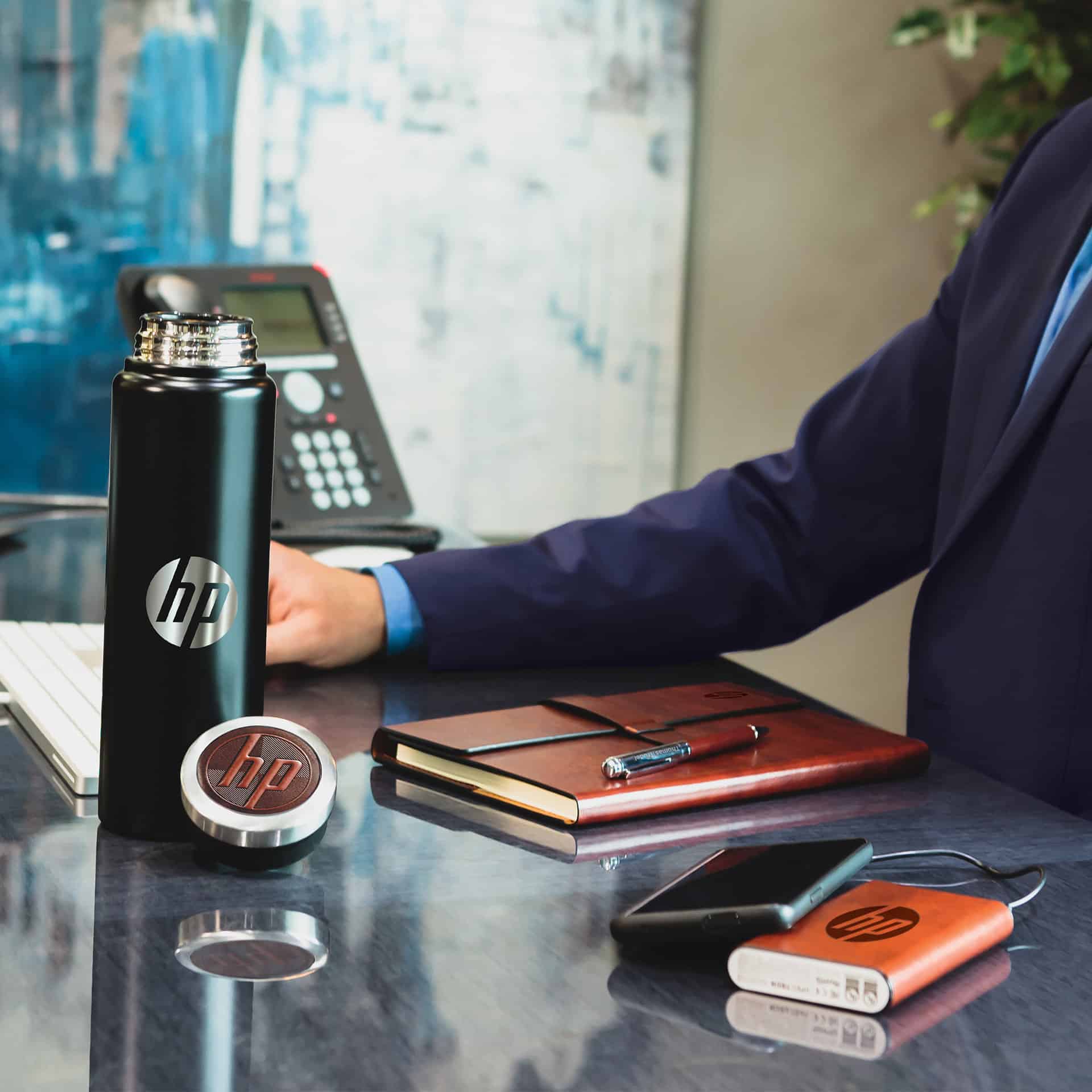 A man in a sharp suit sitting at a desk with a branded water bottle and power bank.