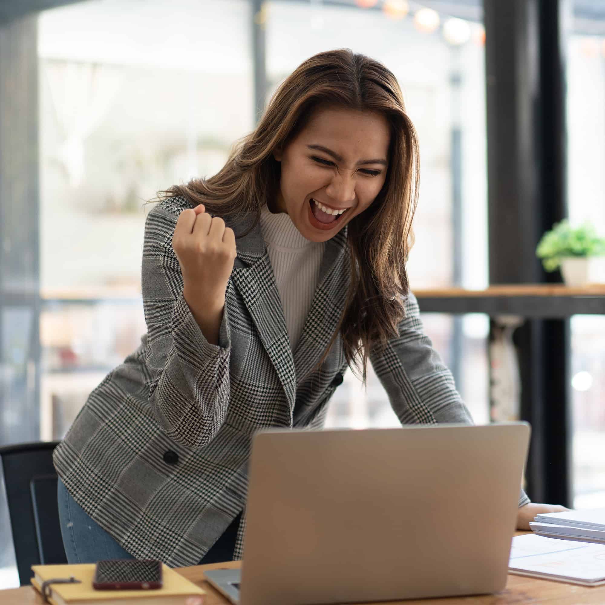 A woman is celebrating while working on a laptop.