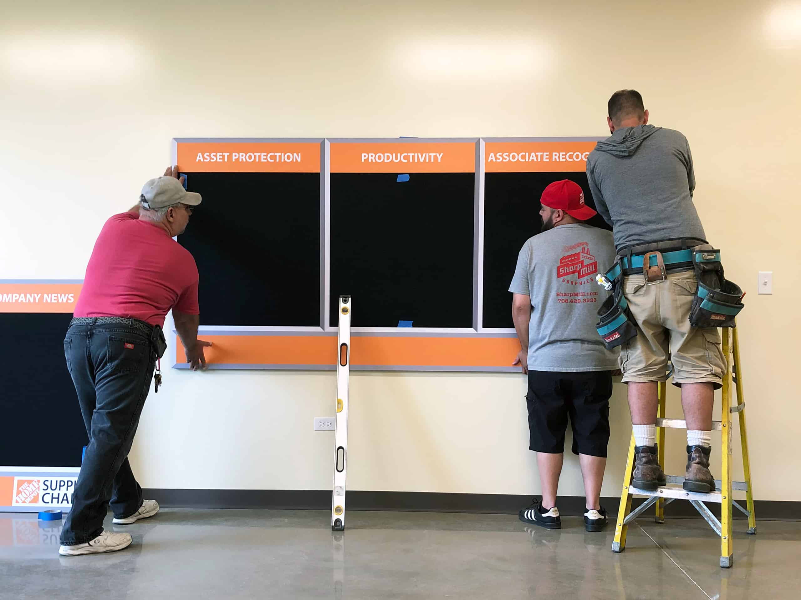 Two men installing a bulletin board.