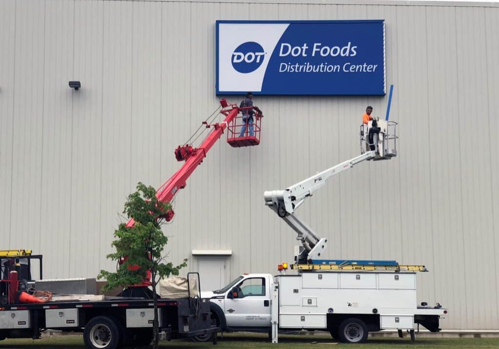 A crane lifts a fulfillment sign in front of a building.